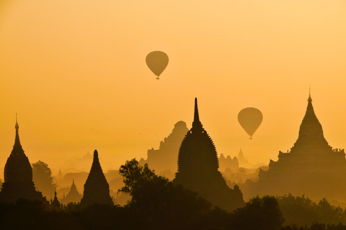 Eine schöne Abendaufnahme von Heißluftballons, die über eine Stadtsilhouette fliegen