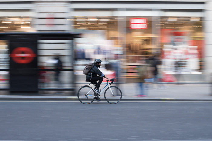 Una persona che va in bicicletta in città, lo sfondo è una sfocatura creativa dovuta all'uso di un tempo di posa lento