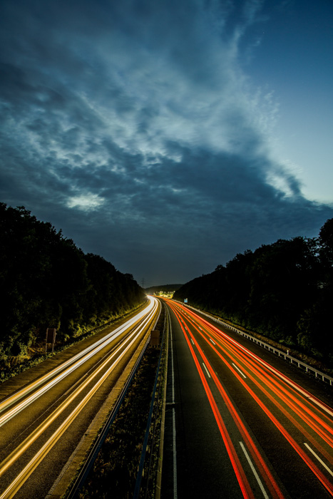 Vista aérea de uma rodovia à noite com faixas de luzes coloridas de carros 