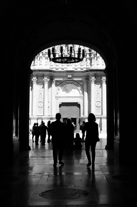 Een zwart-wit straatfoto van mensen die onder een boog door lopen