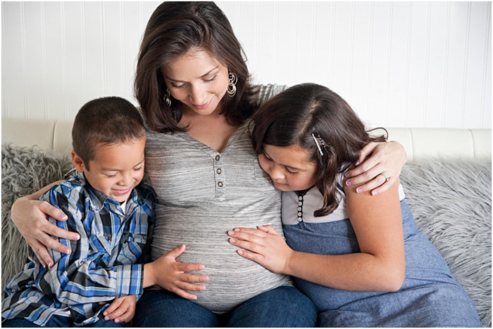 Bidikan fotografi bersalin yang indah dari dua anak, laki-laki dan perempuan, melihat dan menyentuh perut ibu hamil