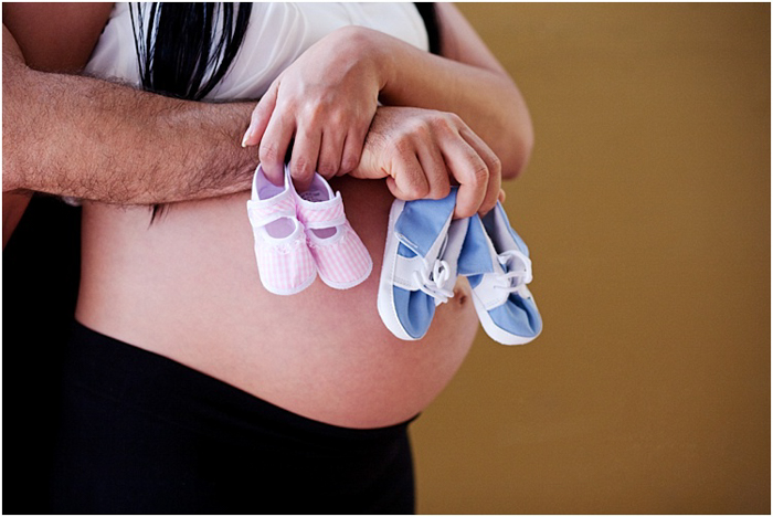 pasangan dekat memeluk perut hamil, memegang sepatu bayi merah muda dan biru