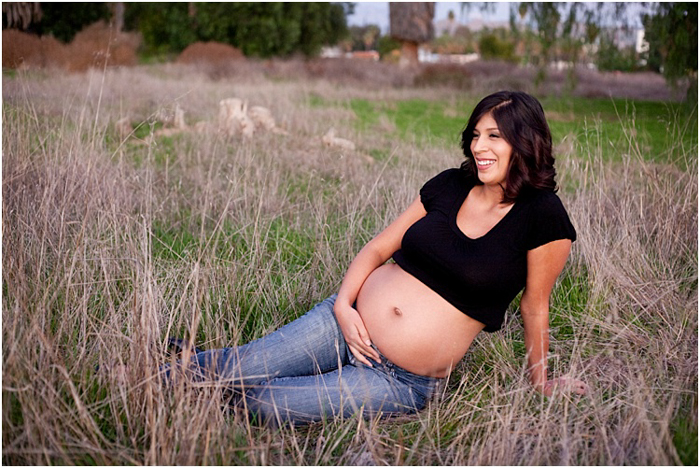wanita hamil dengan jeans dan kemeja hitam, duduk di lapangan sitting