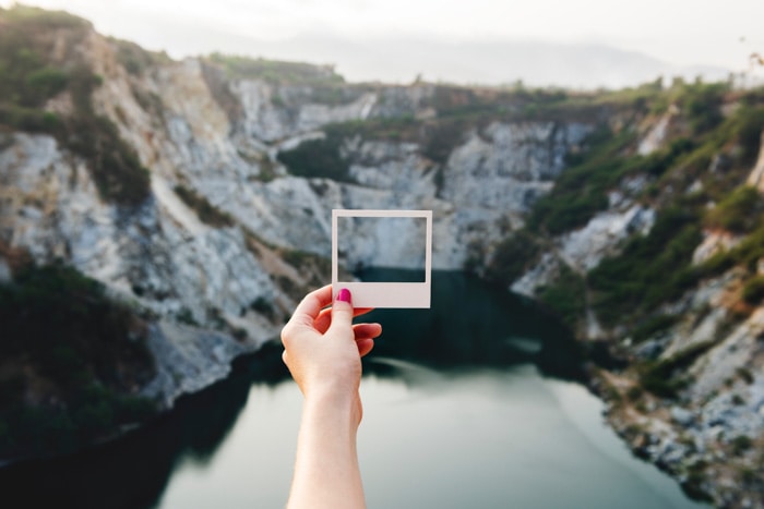Un fotógrafo que sostiene un marco Polaroid contra un paisaje montañoso sobre un lago