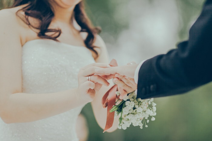 Verträumtes Hochzeitsporträt einer Braut, die einen Ring auf den Finger des Bräutigams legt