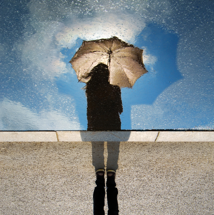 Foto criativa de uma pessoa segurando um guarda-chuva refletida em uma janela respingada de chuva 