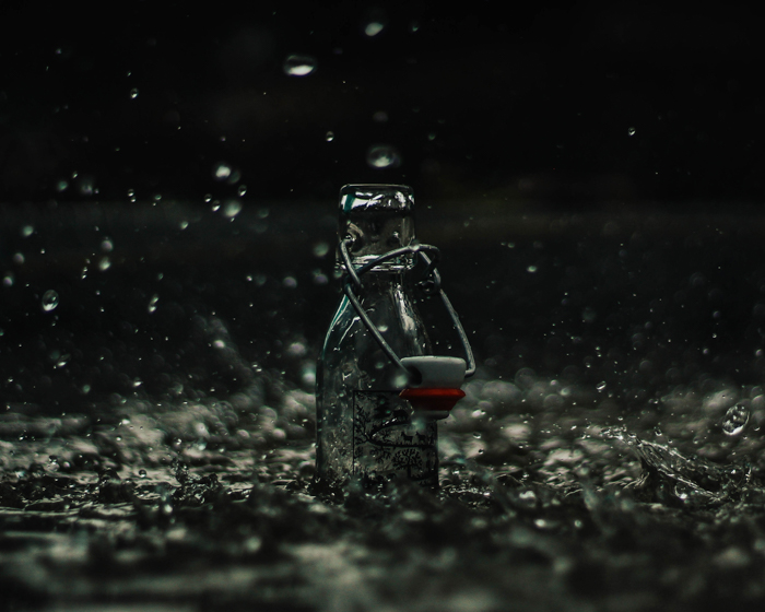 Atmospheric product photography of glass bottle splashed with falling rain