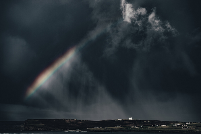 A dramatic landscape with a rainbow breaking through a stormy sky