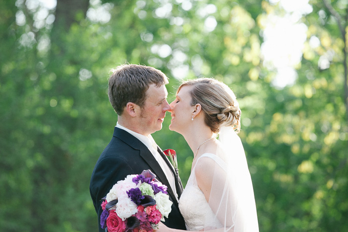 A smiling bride and groom outdoors against a backdrop of green leaves about to kiss - best wedding photo editing tips