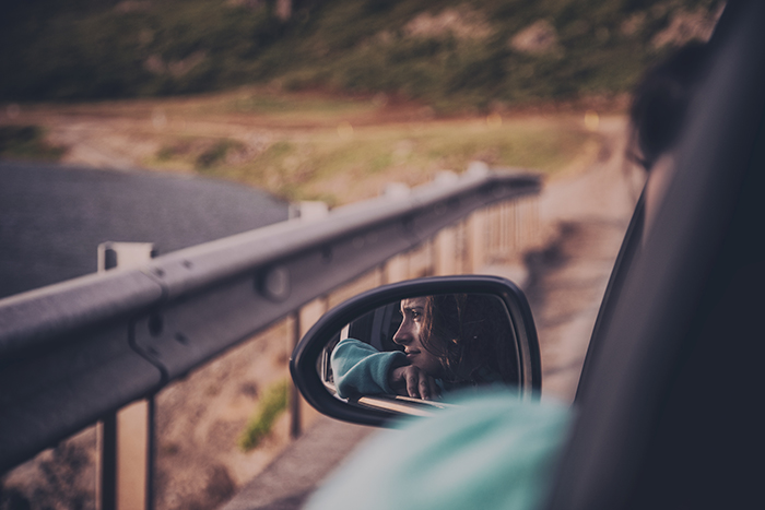 the reflection of a young woman in the side mirror of a driving car 