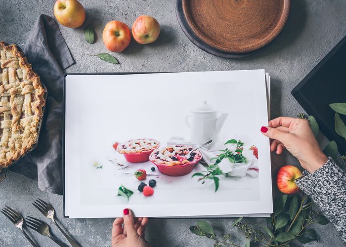 mãos segurando comida fotográfica imprime em uma mesa com maçãs e um bolo 