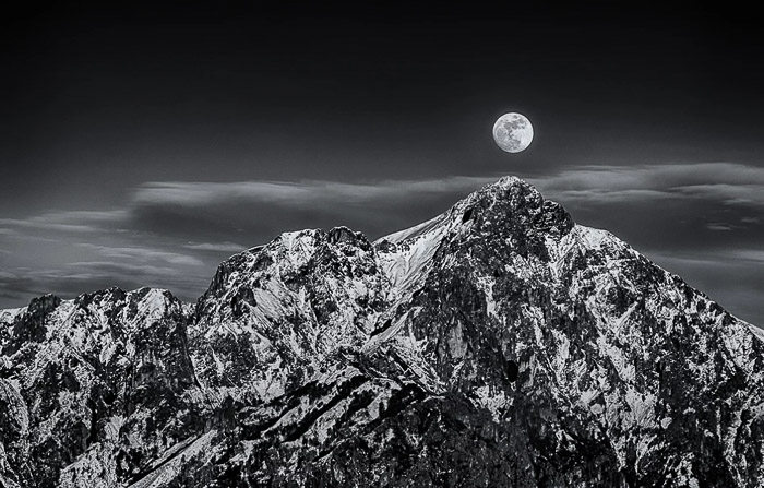 Toma en blanco y negro de la luna llena sobre un impresionante paisaje montañoso