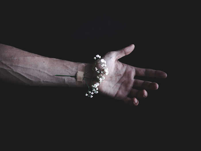 Une photo conceptuelle sombre et lunatique d'une fleur bandée au poignet d'une personne