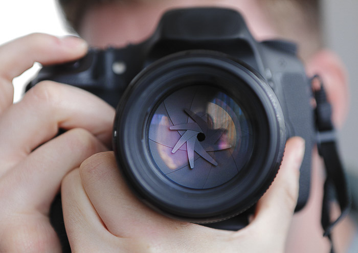 Uma aproximação de um fotógrafo que tira uma fotografia com uma DSLR para mostrar a abertura - diferentes partes da câmara