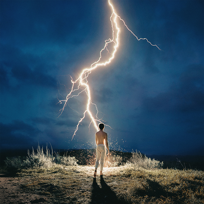 An impressive portrait of a man standing under a lightning bolt by fine art photographer Alex Stoddard