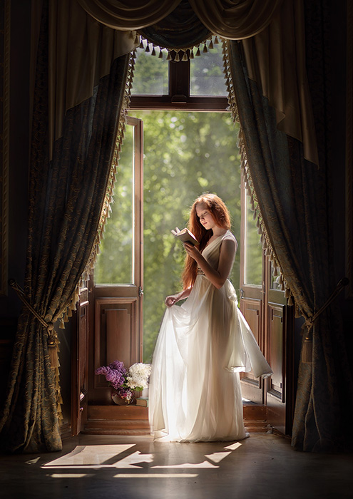 A dreamy fine art photography portrait of a female model reading at a windowsill by fine art photographer Olga Fler
