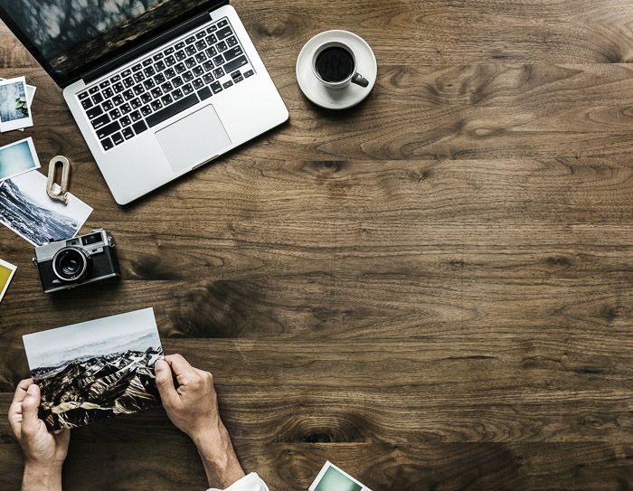 Een overheadshot van een laptop, koffie en een persoon die foto's bekijkt