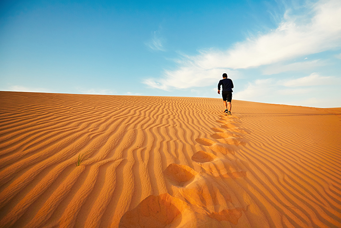 Un jeune homme court vers le sommet d'une dune dans le désert.