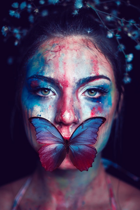 Femme au visage peint et un papillon sur la bouche