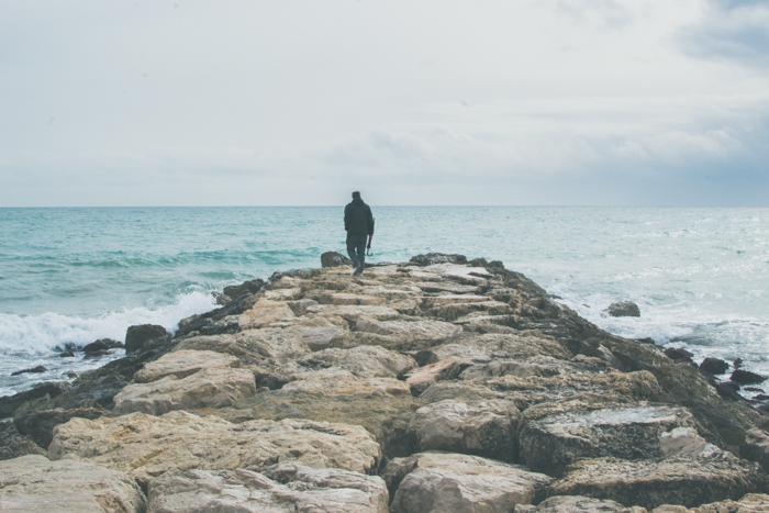 helder en luchtig beeld van een man die naar de zee loopt op een rotsachtige pier - focal point Fotografie