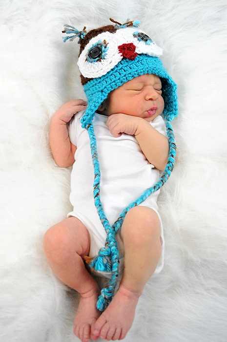 Potret bayi di atas kepala yang manis dengan topi baru di atas selimut putih - fotografi bayi baru lahir