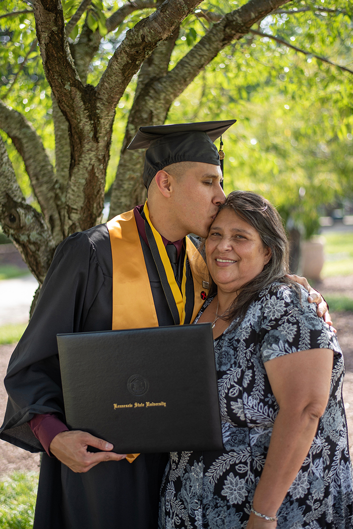 Bela retrato de graduação de um estudante masculino abraçando sua mãe ao ar livre