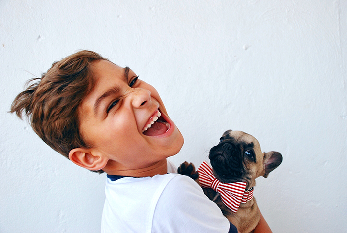 Sjovt portræt af en grinende ung dreng, der holder en lille hund - smilende mennesker