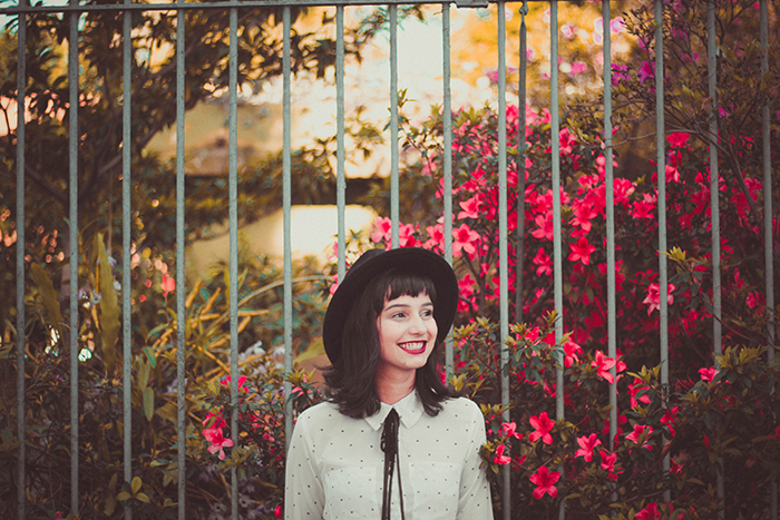 En kvindelig model, der står udendørs foran blomster og smiler naturligt - sådan smiler du på billeder