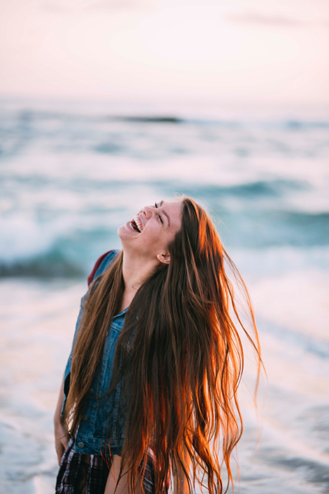 Lustiges Porträt eines lachenden weiblichen Models, das sich die kastanienbraunen Haare schüttelt - wie man für Fotos lächelt