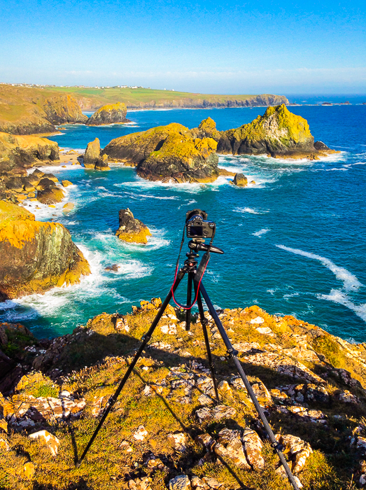 a tripod and dslr set up by a stunning coastal landscape