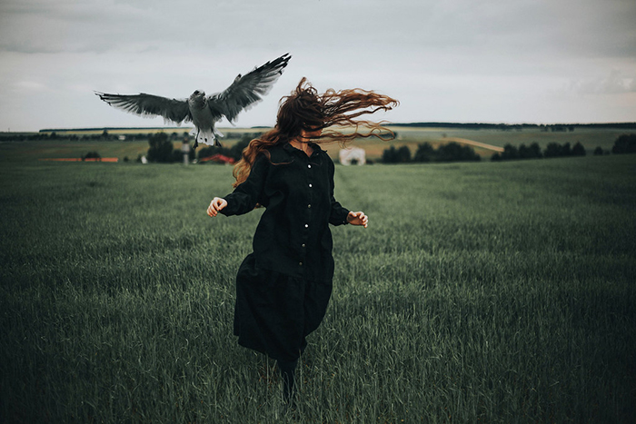 Photo of a woman running on a field with a bird flying beside her