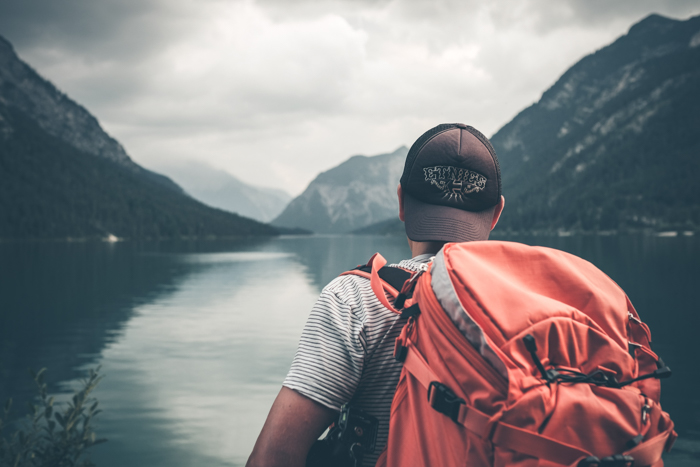 Photo of a guy with a backpack standing on the side of a lake