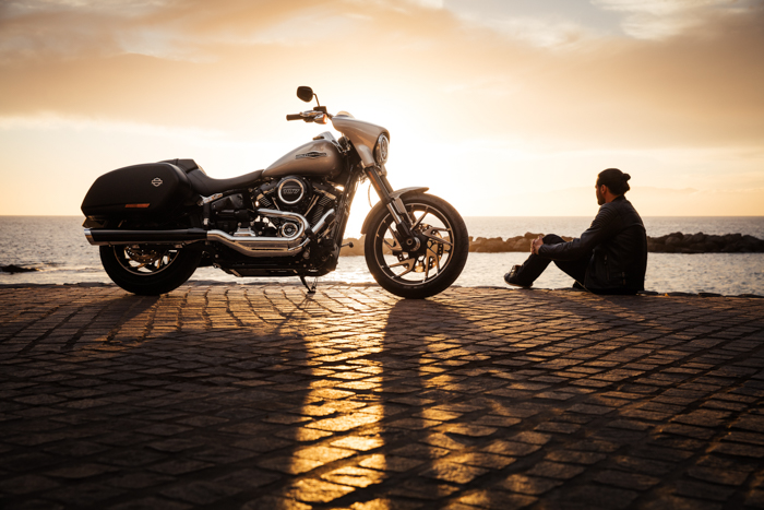 Photo of a man sitting on a seaside with a motorbike