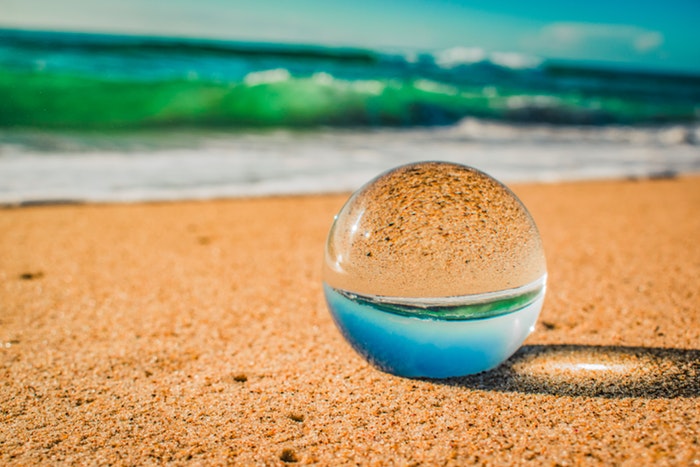 Uma foto de uma bola de cristal na praia refletindo o mar e a areia.