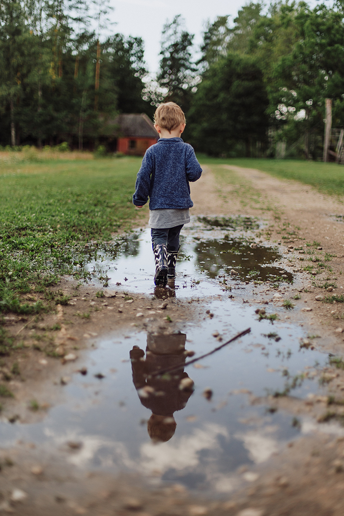 Foto seorang anak kecil dengan sepatu bot berjalan di jalan tanah