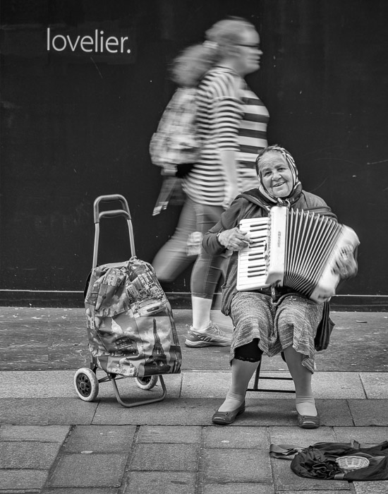 Una mujer tocando el acordeón en la calle con el texto 'lovelier' sobre su cabeza'lovelier' above her head 