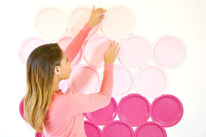 Une femme qui pose des assiettes en papier roses sur un mur
