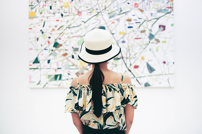 Uma garota com um chapéu preto e branco olhando para uma pintura abstrata