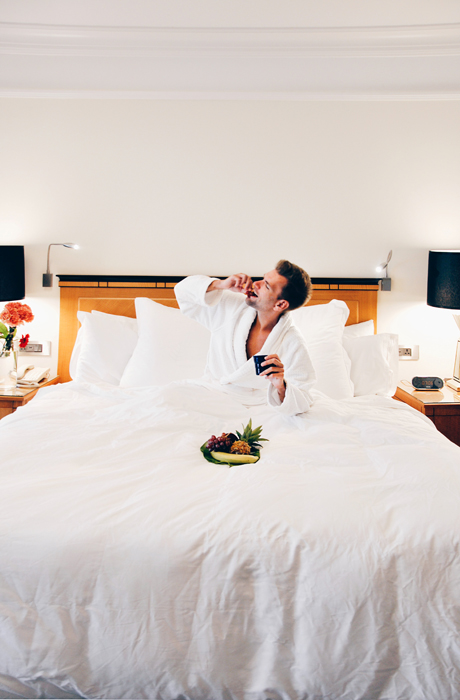 Seorang pria di tempat tidur hotel makan dari semangkuk buah-buahan segar