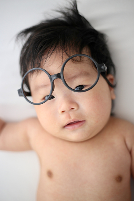 Bayi menggemaskan dengan kacamata bulat dan rambut hitam berantakan