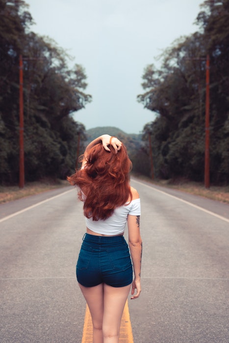 Uma garota de costas para a câmera em uma estrada.