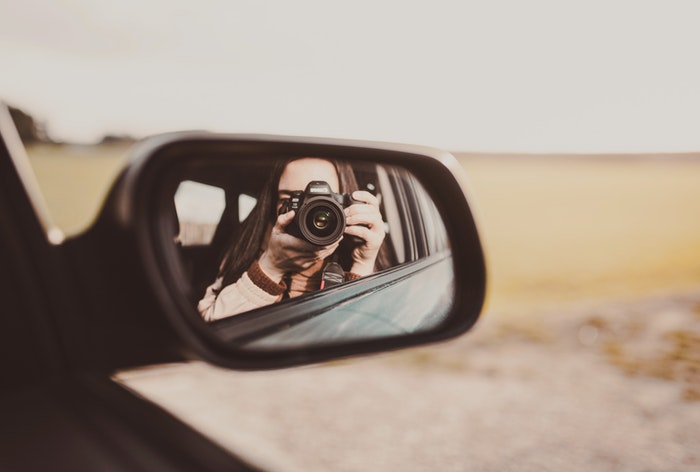 Uma garota fazendo um autorretrato no espelho lateral de um carro