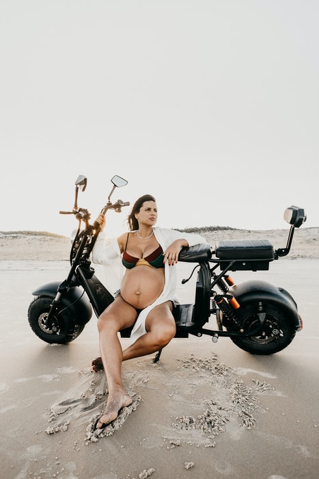 Seorang wanita hamil berpose dalam pakaian dalam di atas sepeda motor