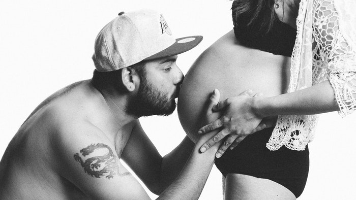 Foto kamar kerja bersalin hitam putih seorang pria mencium perut istrinya yang sedang hamil