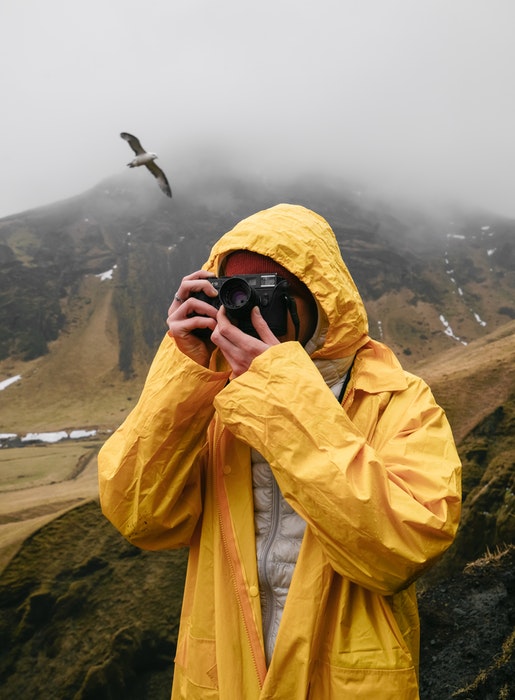 um fotógrafo em amarelo fotografando em um dia chuvoso nas montanhas com um pássaro atrás dele