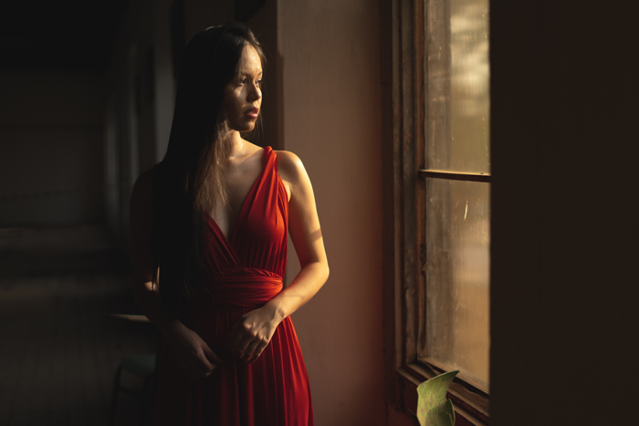 Foto de uma mulher com um vestido vermelho em pé perto da janela e olhando para fora
