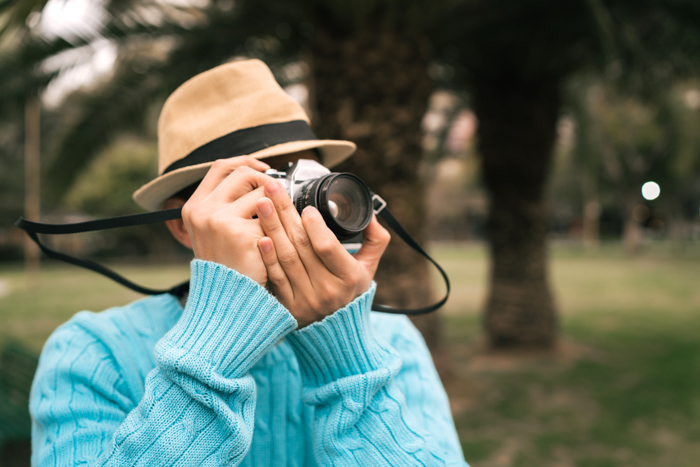 Retrato de um jovem turista asiático usando uma câmera vintage e tirando algumas fotos ao ar livre na rua. 