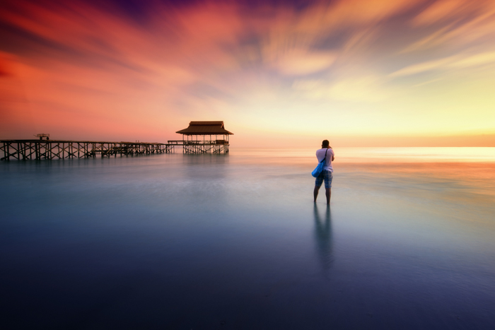 Foto de longa exposição de um fotógrafo em uma praia ao pôr do sol