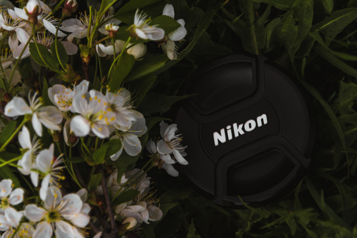 Closeup atas tutup lensa Nikon di antara bunga