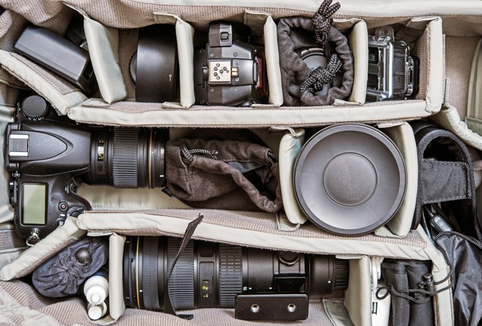 Uma imagem de aparelhos fotográficos e equipamentos fotográficos em uma bolsa fotográfica.